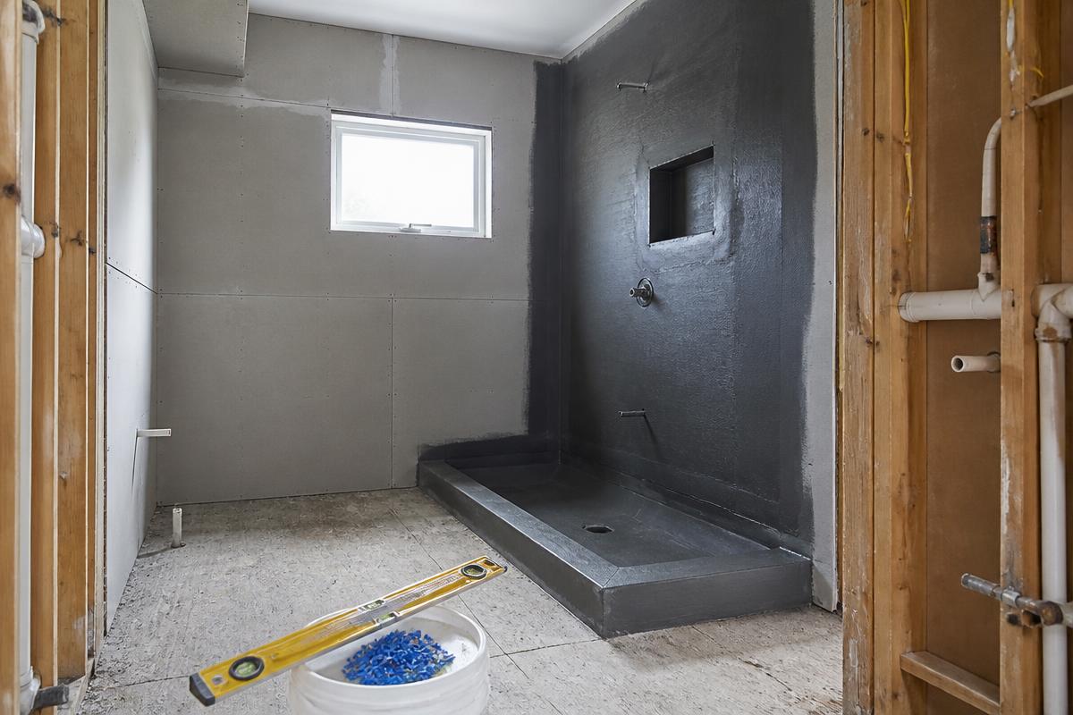 Bathroom renovation in progress with cement backer board, a waterproofed shower pan and exposed plumbing