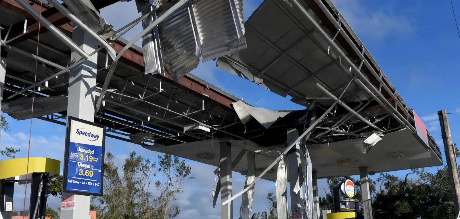 Hurricane-torn gas station canopy with twisted metal roofing panels hanging over the pumps, illustrating wind damage from Hurricane Isaias.