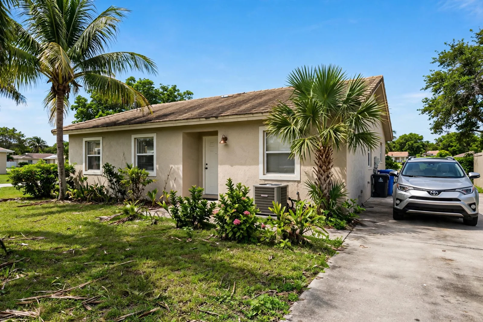 Single-story stucco family home in South Florida with palm trees, a shingle roof, and an SUV in the driveway on a sunny day